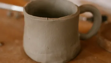 Unfinished clay mug on wooden table.