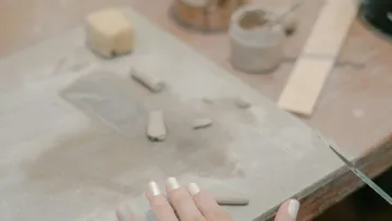 Hand arbeitet mit Tonstücken auf Tisch.