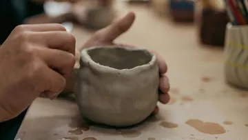 Hände formen Tonkrug auf einem Tisch.