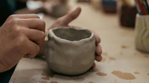 Hands shaping a clay pot on table.