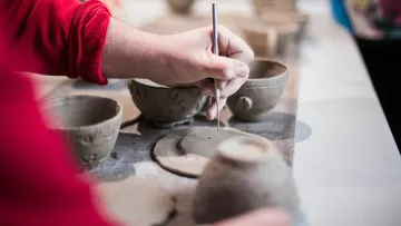 Hand carving details into clay bowl, studio.