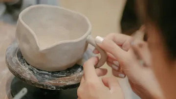 Person shaping clay mug handle in pottery studio.