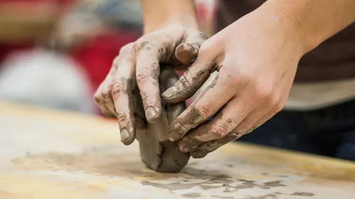 Hands shaping clay on a wooden table.