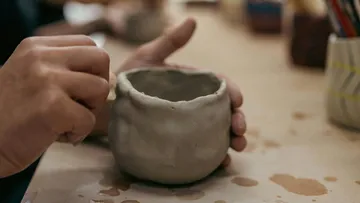 Hände formen Tonbecher auf Tisch.