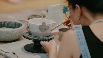 Person decorating pottery bowl with flowers.