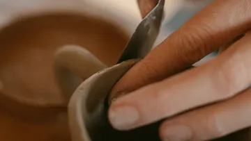 Person shaping clay pottery with hands.
