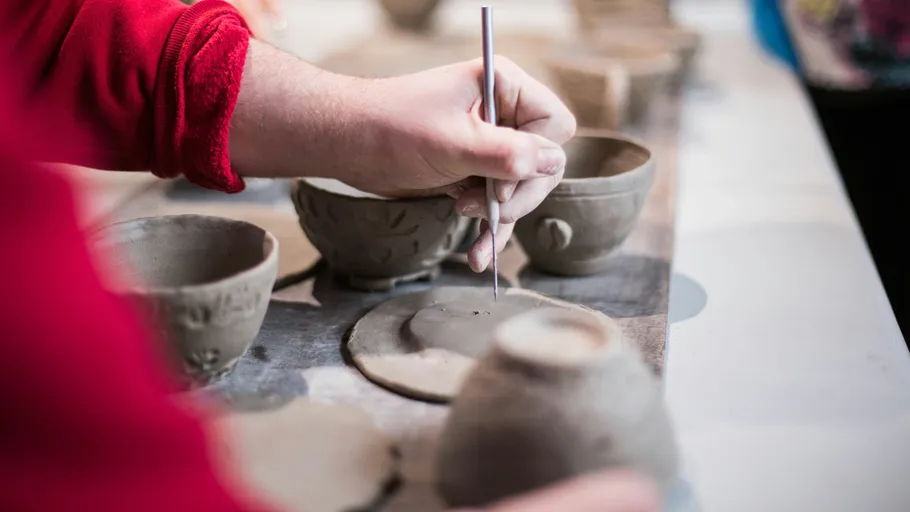 Person carving pottery on a table.