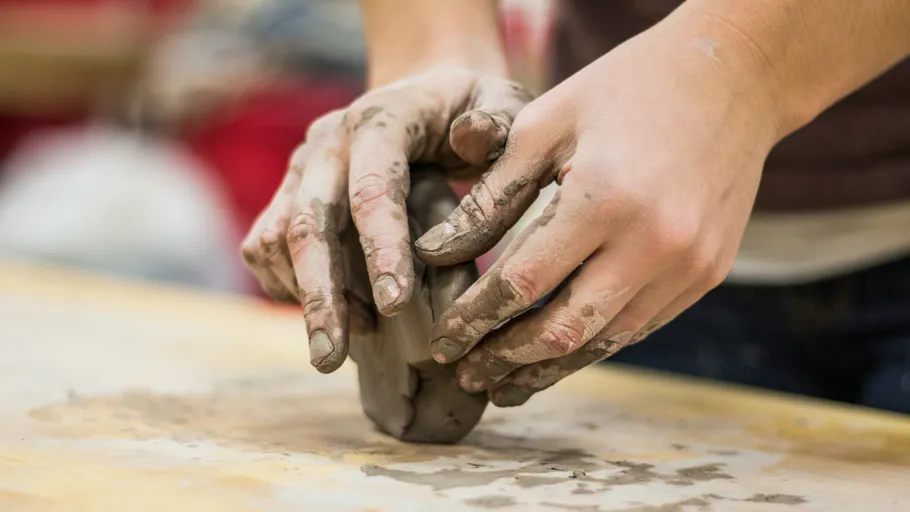 Hands shaping clay on a wooden surface.