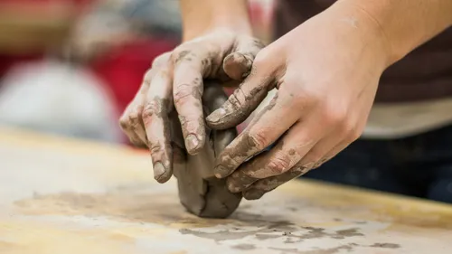 Hands shaping clay on a wooden table.