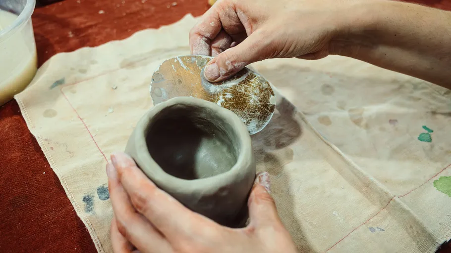 Hands shaping clay pot on canvas cloth.