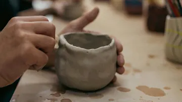 Hands shaping clay pot on table.