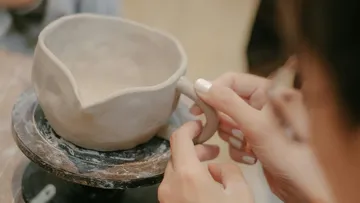 Hands shaping clay cup on pottery wheel.