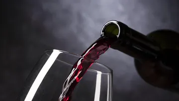 Rotwein wird in ein Glas gegossen, dunkler Hintergrund.