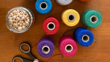 Bunte Garnrollen, Schere und Perlen auf Tisch.