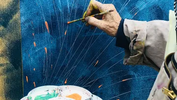 Künstler malt mit Pinsel auf blauer Leinwand.
