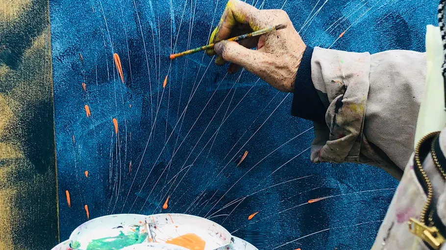 Artist painting on blue canvas with brush.