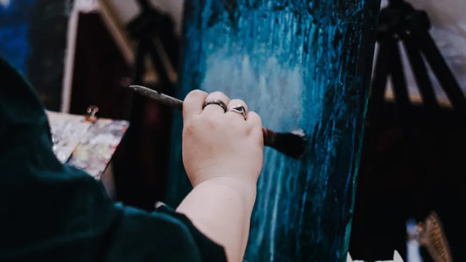 Person painting blue artwork on canvas.