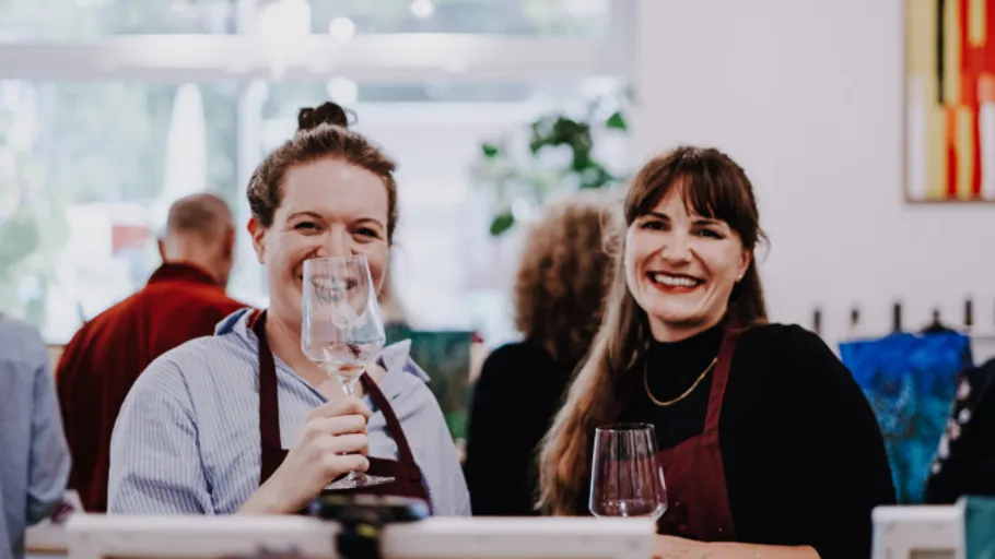 Two women smiling, holding wine glasses indoors.