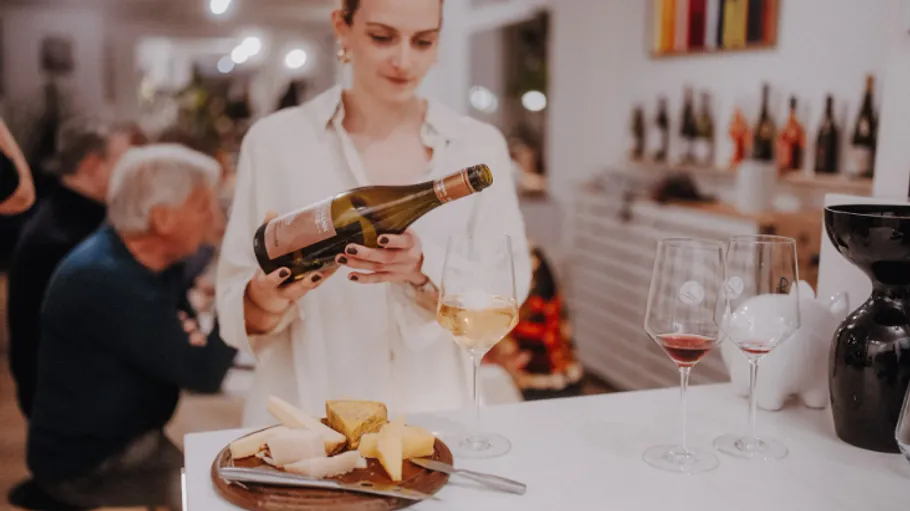 Woman examining wine bottle near glasses and cheese.