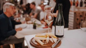 Cheese and wine on table, people dining background.