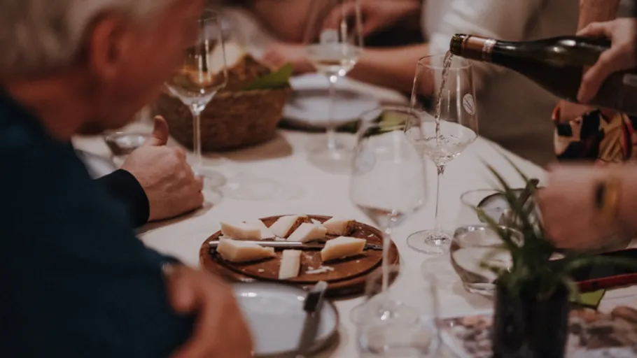 Wein wird am Tisch mit Käseplatte eingeschenkt.