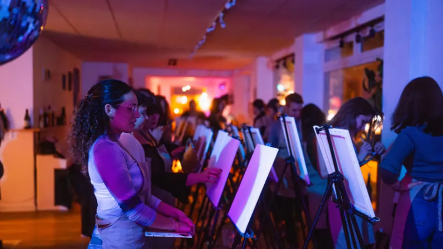 People painting at easels in dimly lit room.