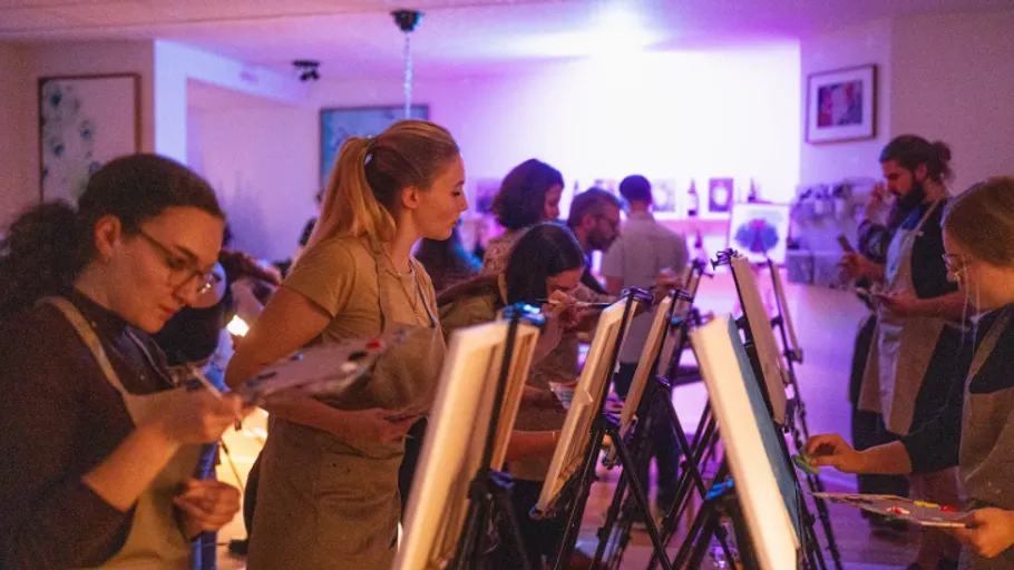 People painting on easels in dimly lit room.