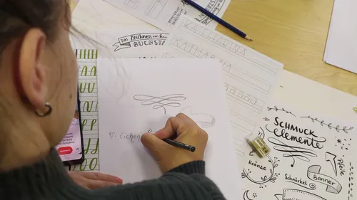 Person zeichnet dekorative Elemente am Schreibtisch.