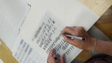 Person übt Kalligraphie am Tisch.