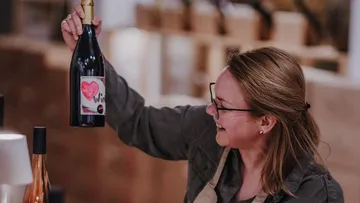 Frau lächelt und hält eine Weinflasche drinnen.