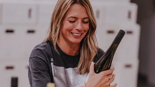 Woman smiling while holding wine bottle indoors.