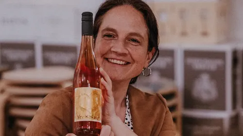 Woman holding a bottle of wine, smiling indoors.