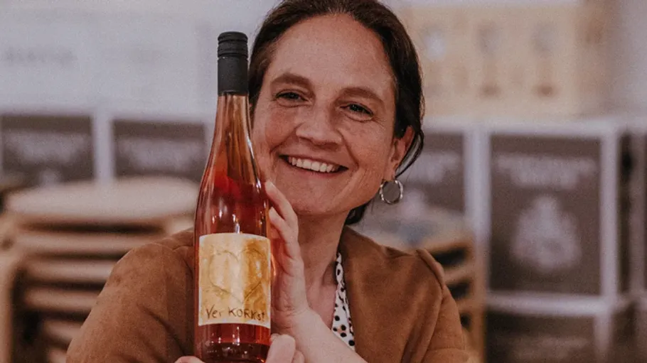 Woman holding a bottle of wine, smiling indoors.