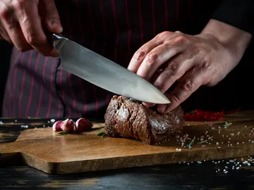 A cook cuts meat on a wooden board.