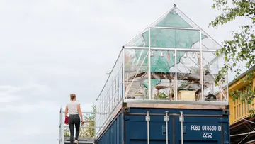 Person geht auf Gewächshaus auf Container zu.