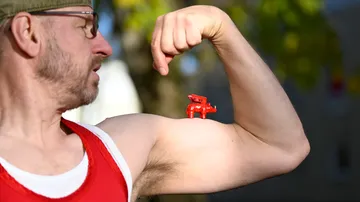Man flexing bicep with red toy pig.