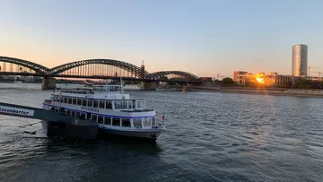 Boat docked near arches on river at sunset.