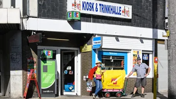 Zwei Personen mit Wagen vor Kiosk.
