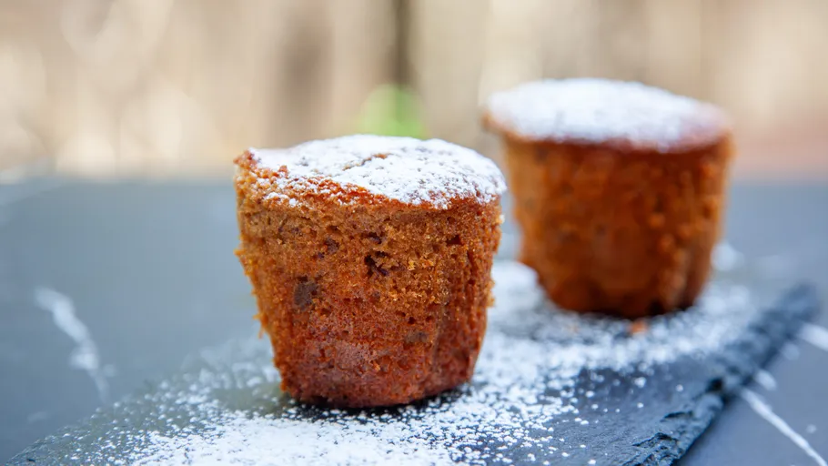 Two muffins with powdered sugar on slate.