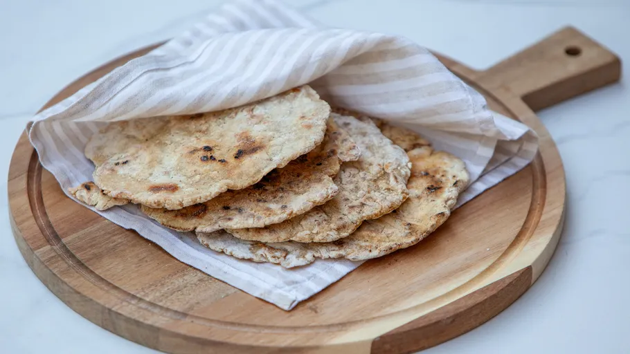 Flatbreads on wooden board under striped cloth.