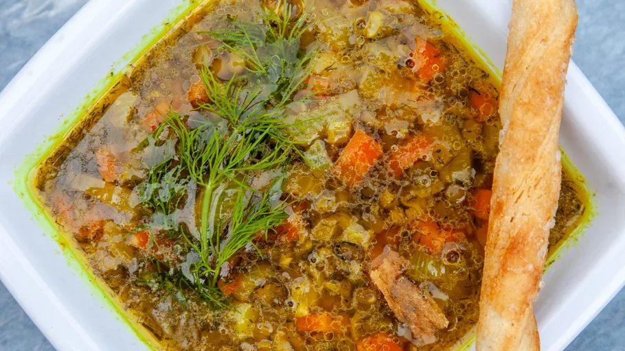 Vegetable soup with breadstick on plate.