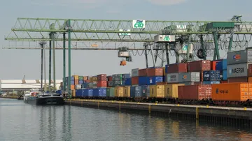 Schiffscontainer gestapelt nahe Wasser und Kränen.