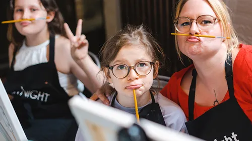 Three people balancing pencils under noses indoors.