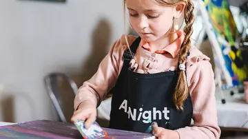 Girl painting with brush at table indoors.