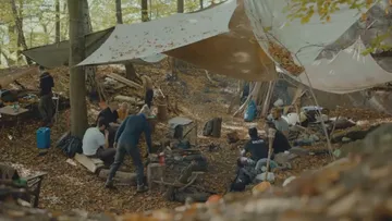 People gathered in a forest camp setting.