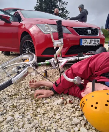 Man lies by bicycle, car parked nearby.