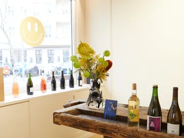 Vase with flowers is on a wooden table, bottles next to it.