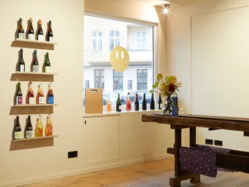Bottles stand on shelves and window sills in simple rooms.