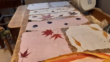 Handcrafted paper with pressed leaves on table.