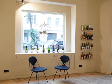 There are two chairs next to a window with bottles of wine.